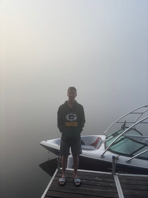 photo of boy in front of speedboat and a foggy lake