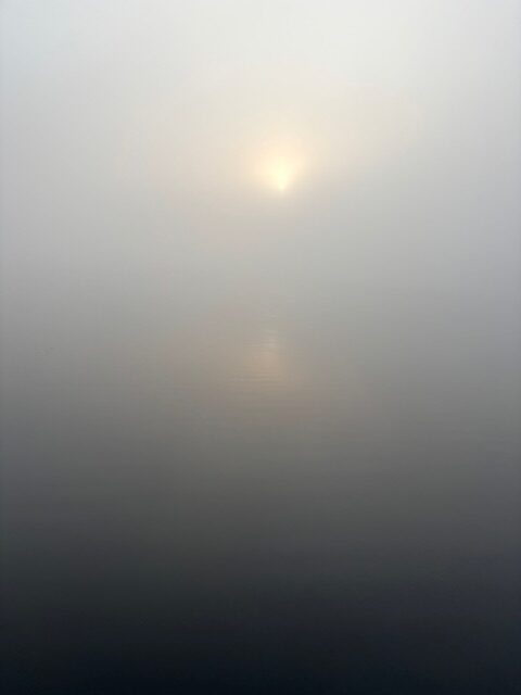 photo of sun trying to shine through fog on a lake